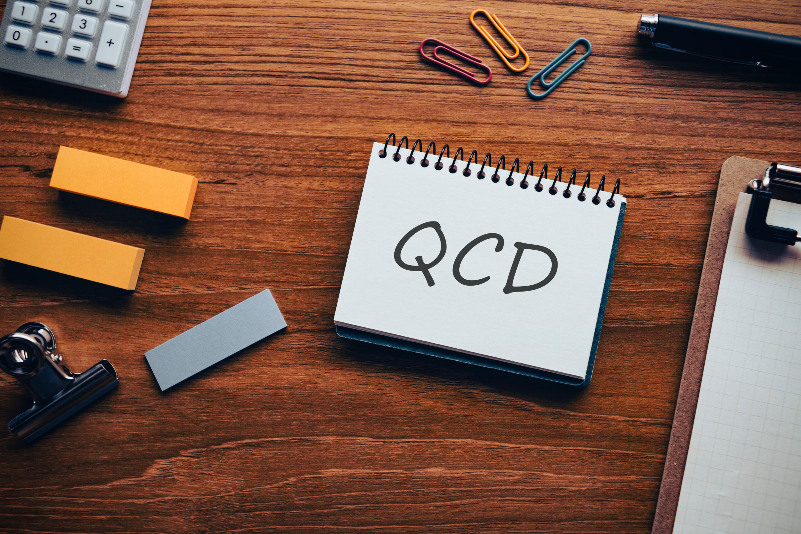 There is notebook with the word QCD. It is an abbreviation for Quality, Cost, Delivery as eye-catching image.