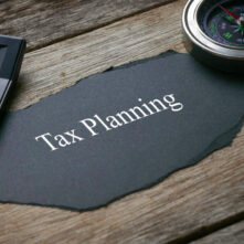Compass,calculator,pen and a piece of black paper written with Tax Planning on wooden background.