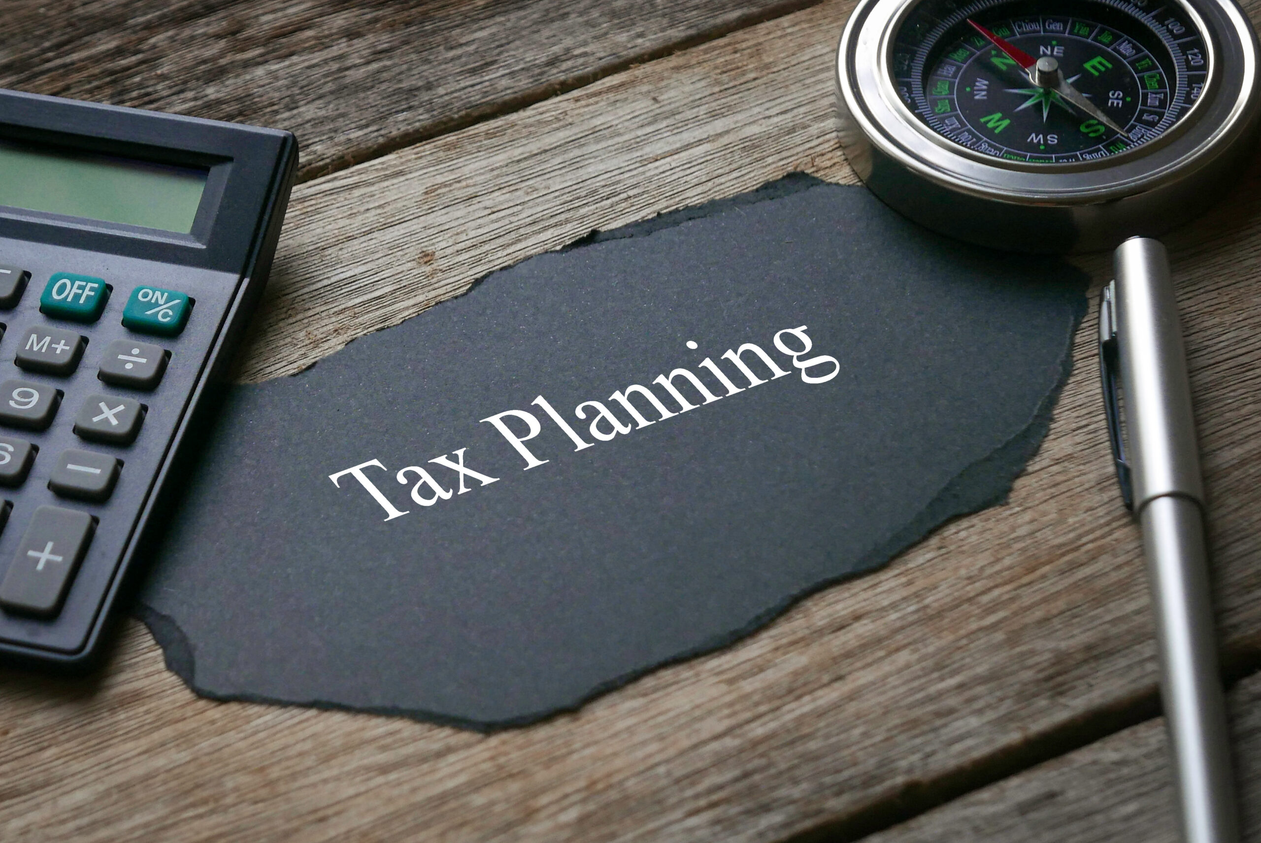 Compass,calculator,pen and a piece of black paper written with Tax Planning on wooden background.
